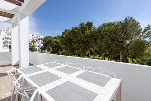 A terrace with a white table and chairs, overlooking a residential area with trees and white buildings. - Golf Gardens Miraflores (Mijas)