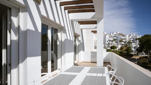 Ein Balkon mit weißen Stühlen und Tischen mit Blick auf ein Wohngebiet mit weißen Gebäuden und Palmen.