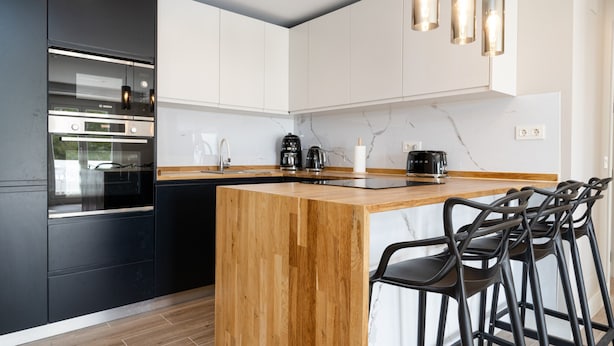 Eine moderne Küche mit einer Holztheke, schwarzen Geräten und Barhocker.