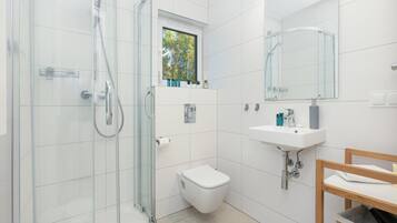 A modern bathroom with a glass-enclosed shower, a toilet, a sink, and a window above the toilet.
