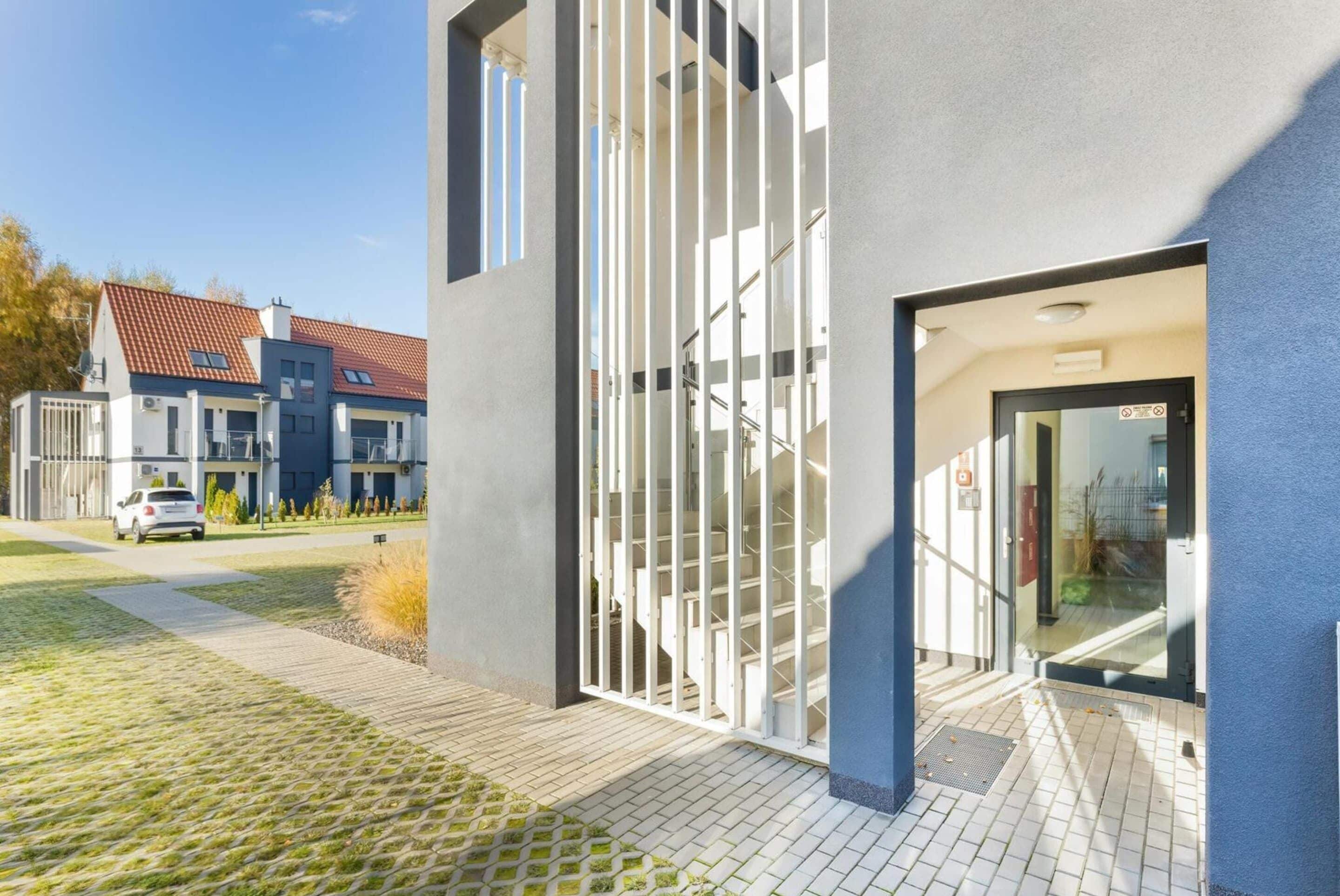 Un edificio moderno con entrada de vidrio, una escalera visible y un camino de entrada pavimentado.