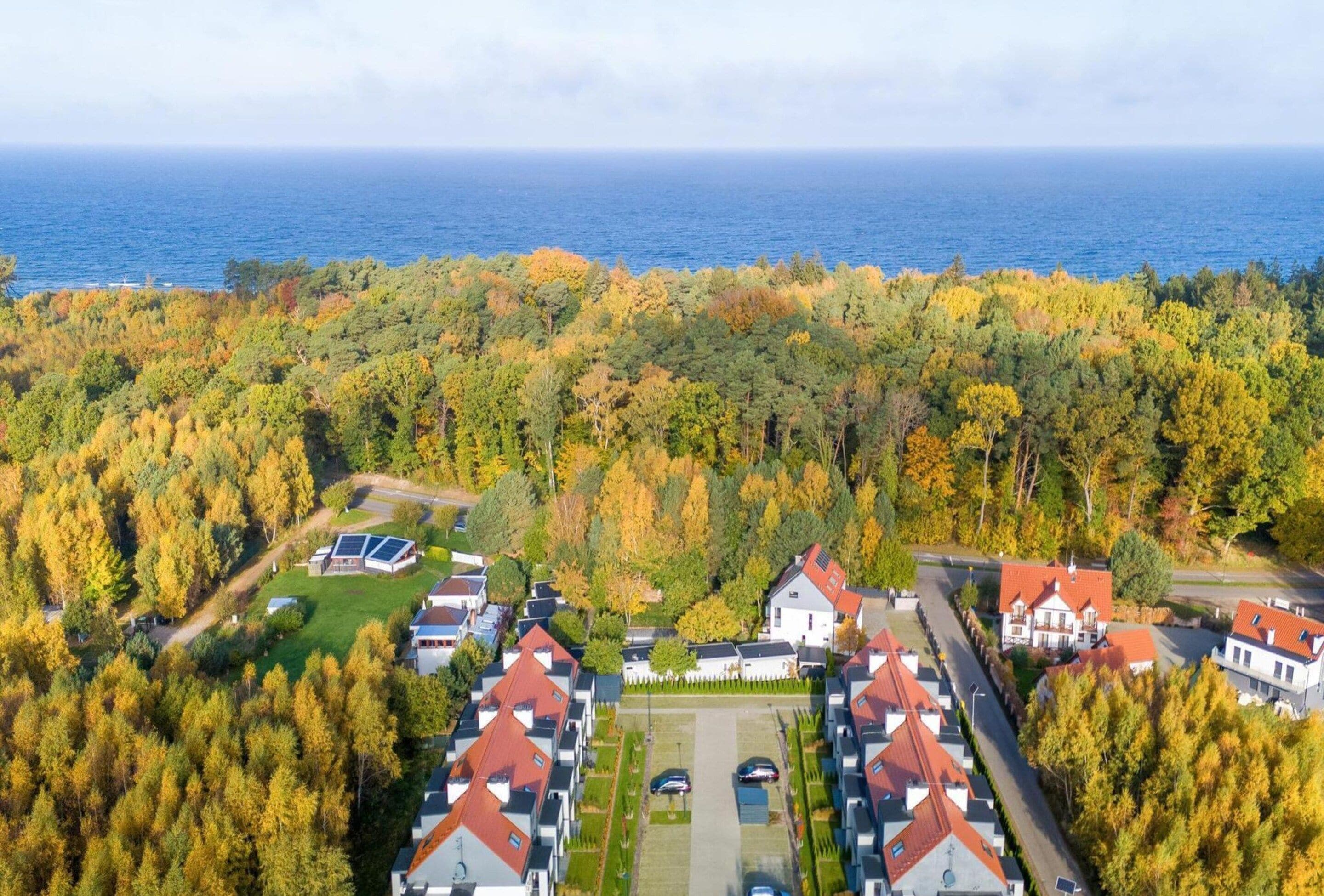 An aerial view of a residential area with houses, a parking lot, and a body of water in the background.
