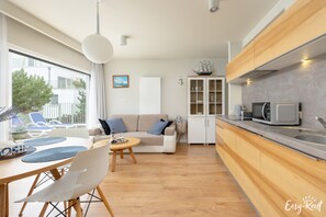 A modern kitchen with wooden cabinets, a microwave, and a dining area with a table and chairs. - Apartment Pogorzelica With SPA Near Baltic Beach (Rewal)