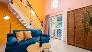 Een woonkamer met een blauwe bank, een klein houten tafeltje en een trap tegen een gele muur.