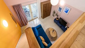 Een moderne woonkamer met een blauwe bank, een houten tv-meubel en een groot raam met gordijnen.