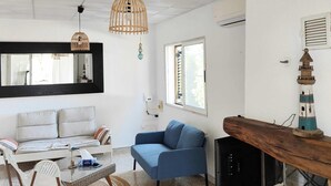 Un saló modern amb un sofà blanc, una butaca blava i una taula de centre de vidre. Hi ha un moble de televisió de fusta amb un televisor i un fanal decoratiu.