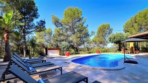 Zona de piscina con sillas de descanso y una pileta, rodeada de árboles y un espacio de descanso cubierto.