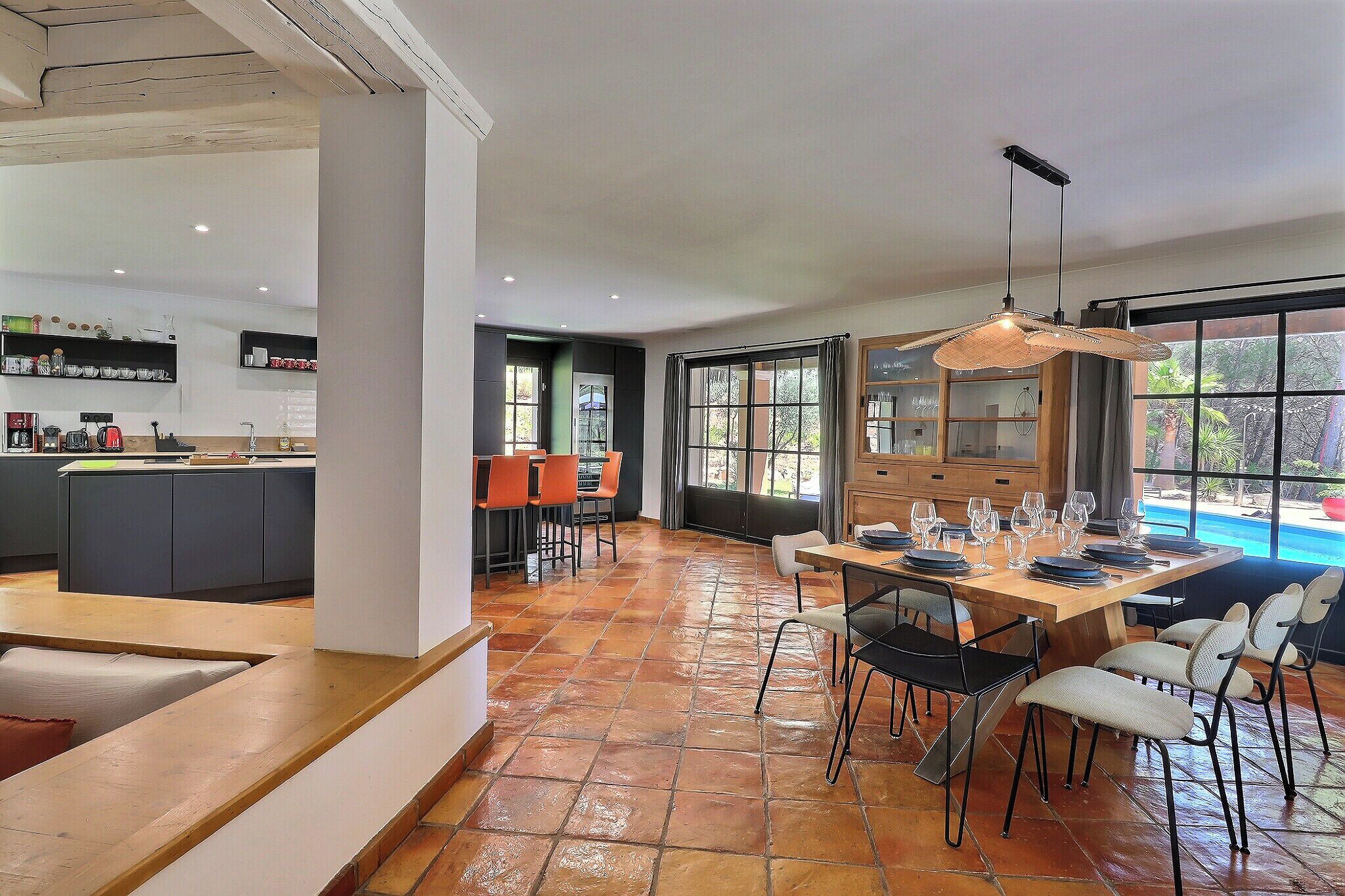 Une cuisine spacieuse dotée d’appareils électroménagers modernes, un coin repas avec une table et des chaises en bois, et de grandes fenêtres offrant une vue sur l’extérieur.