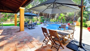 Un patio al aire libre con piscina, sillas de madera y sombrillas.