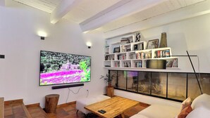 Un salón moderno con un televisor de pantalla plana montado en la pared, una mesa de centro de madera, un sofá blanco y una estantería llena de libros y objetos decorativos.