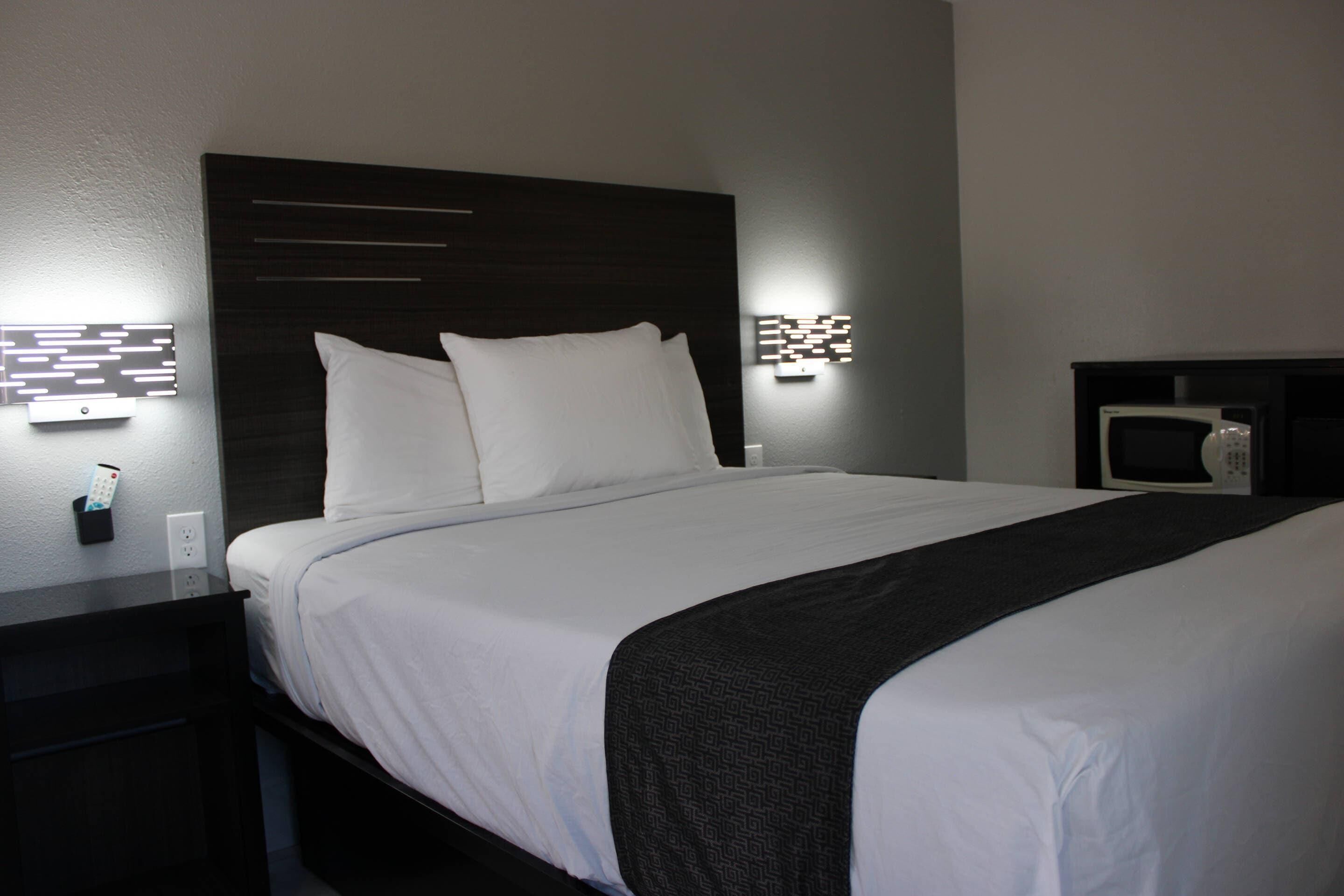 A neatly made bed with white linens and a dark headboard. There are two wall-mounted light fixtures on either side of the bed.