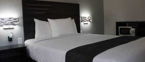 A neatly made bed with white linens and a dark headboard. There are two wall-mounted light fixtures on either side of the bed.