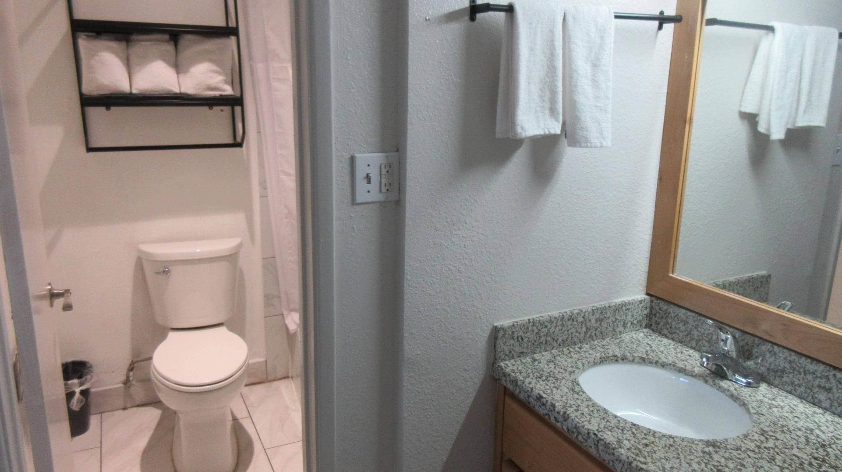 Un baño con inodoro, lavabo y espejo. Hay un perchero con toallas.