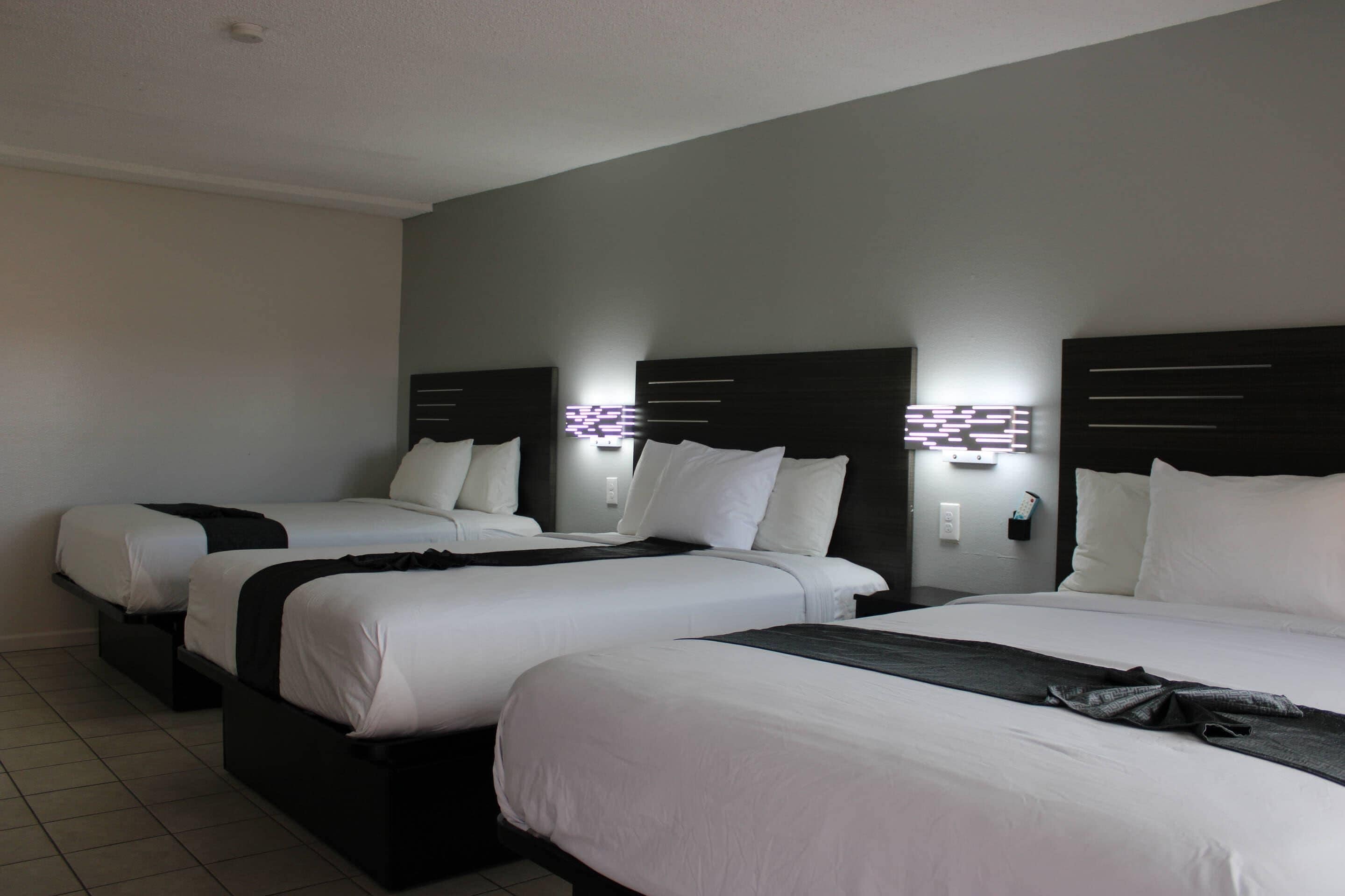 A hotel room with three single beds, each with a black headboard and white bedding.
