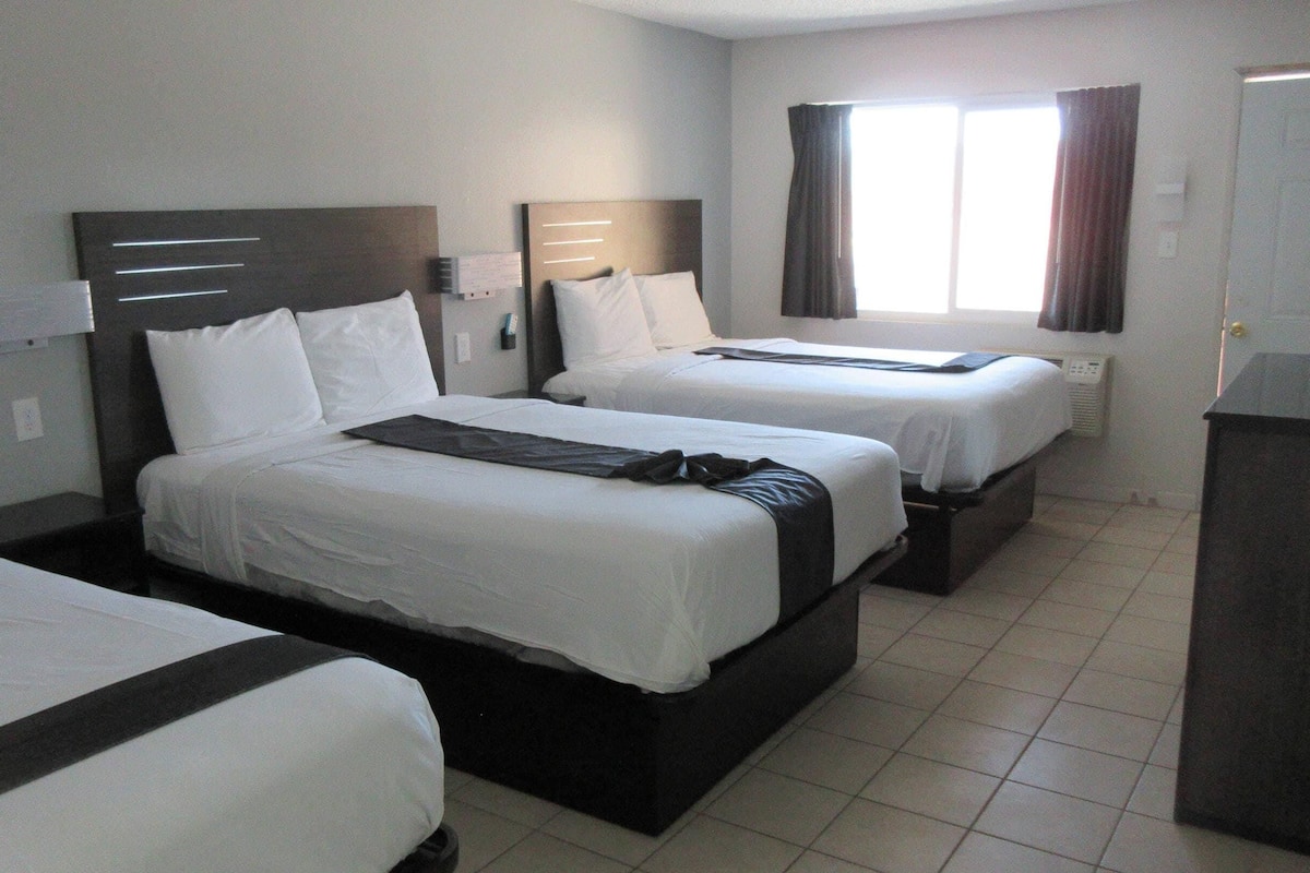 A hotel room with two beds, a window with curtains, a bedside table, and a wardrobe.