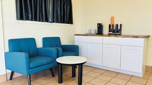 Una stanza piccola con un divano blu, un tavolino rotondo e un armadio bianco contenente una macchina per il caffè e tazze.