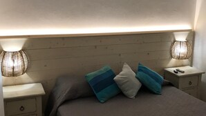 Un llit ben fet amb capçalera, dues làmpades laterals i una tauleta de nit amb un comandament a distància.