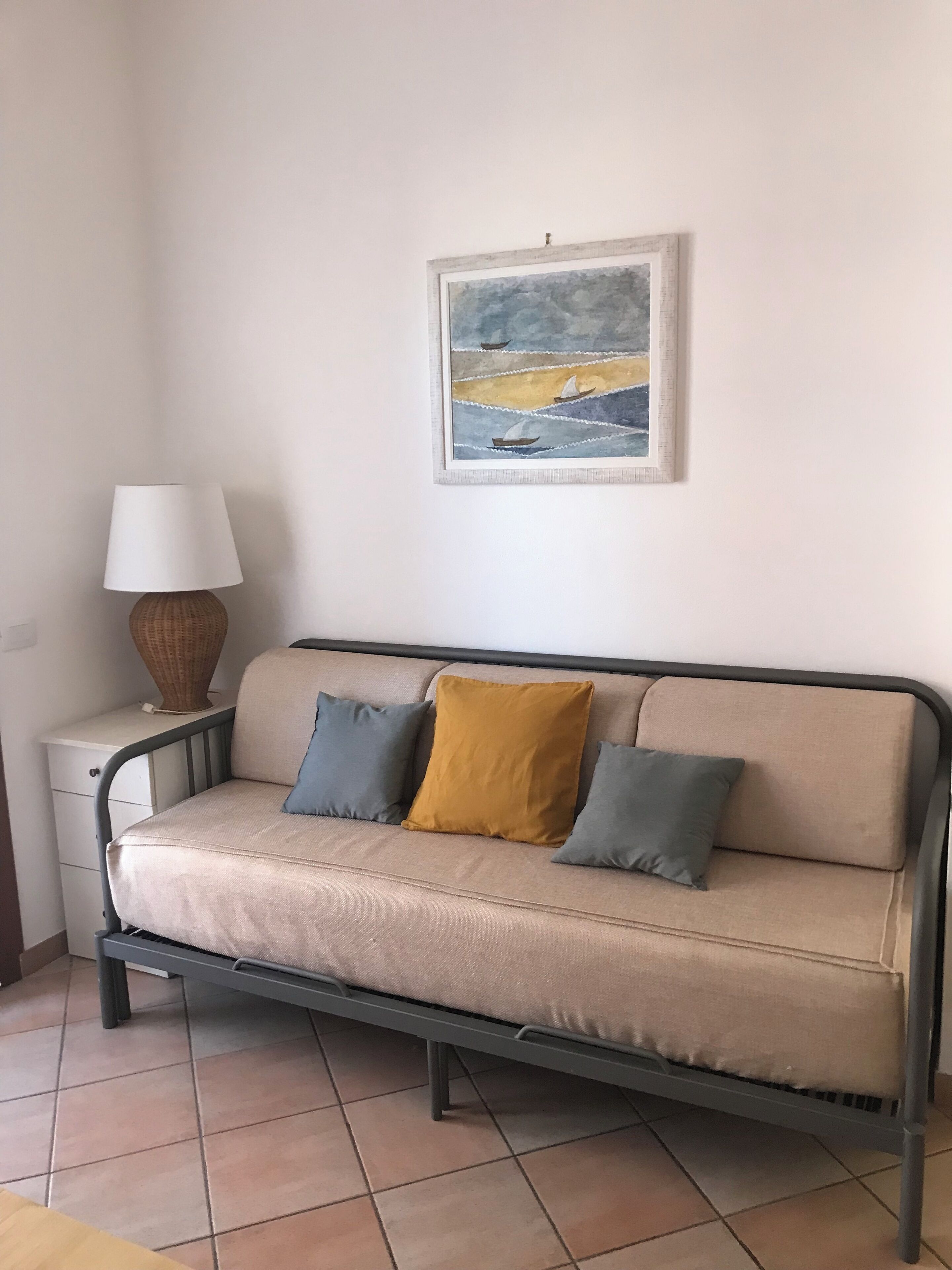 Un canapé beige avec deux coussins, une lampe et un tableau accroché au mur.