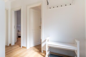 Enter a clean and orderly hallway with a wooden floor and white walls, featuring a bench and coat rack.