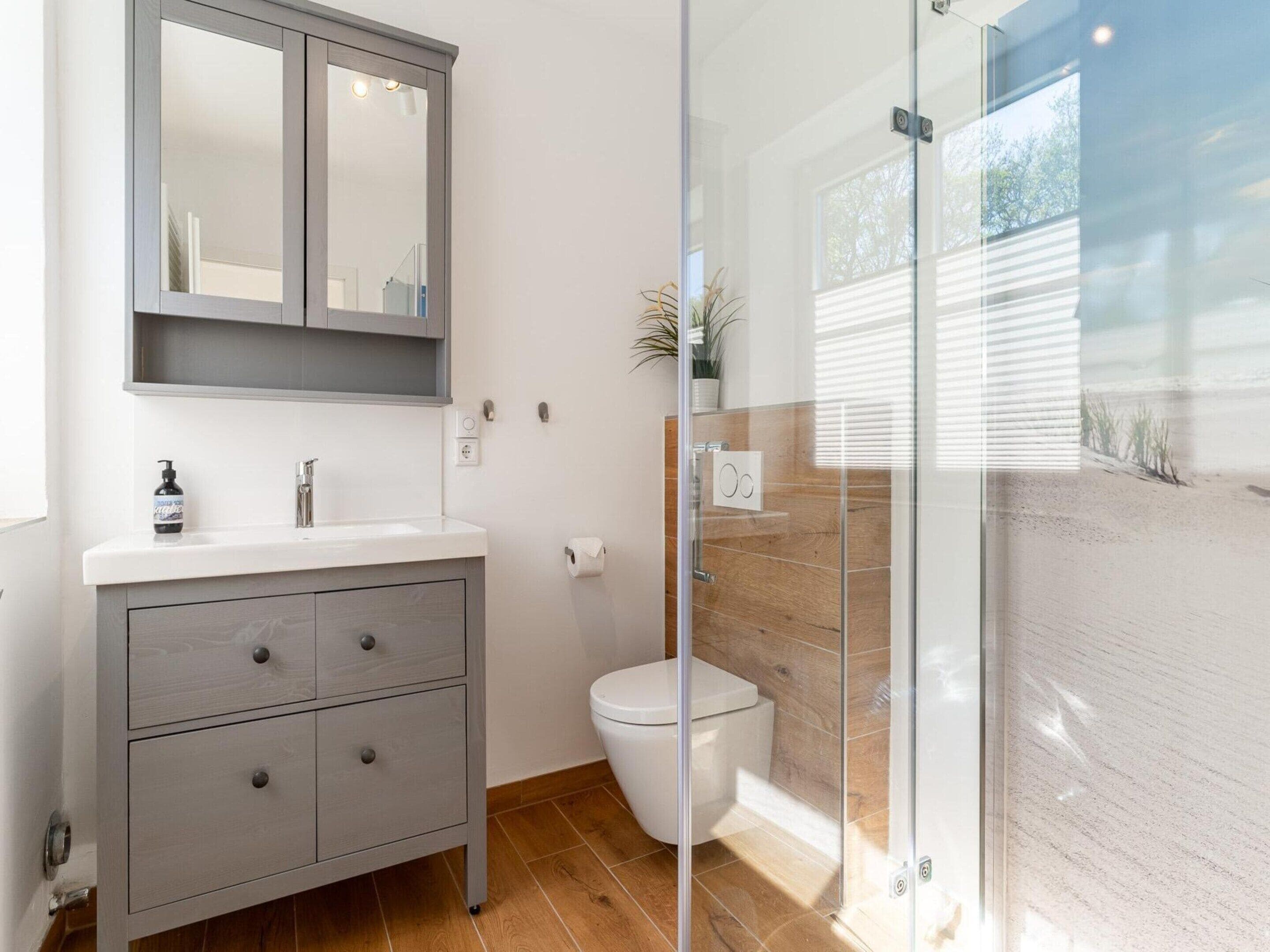 Casa de banho moderna com toucador cinzento, sanita branca e cabine de duche em vidro.