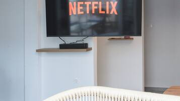 En moderne stue med et ophængt fjernsyn, der viser Netflix-logoet, en træhylde nedenunder og en hvid, vævet stol.