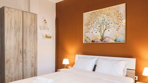 Ein ordentlich bezogenes Bett mit weißen Leinen und Handtüchern, ein Holzschrank, ein Baumgemälde und ein Kronleuchter.