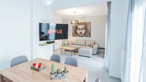 Ein modernes Wohnzimmer mit Flachbildfernseher, einer Couch, einem Couchtisch und einem Essbereich mit Holztisch und Stühlen.