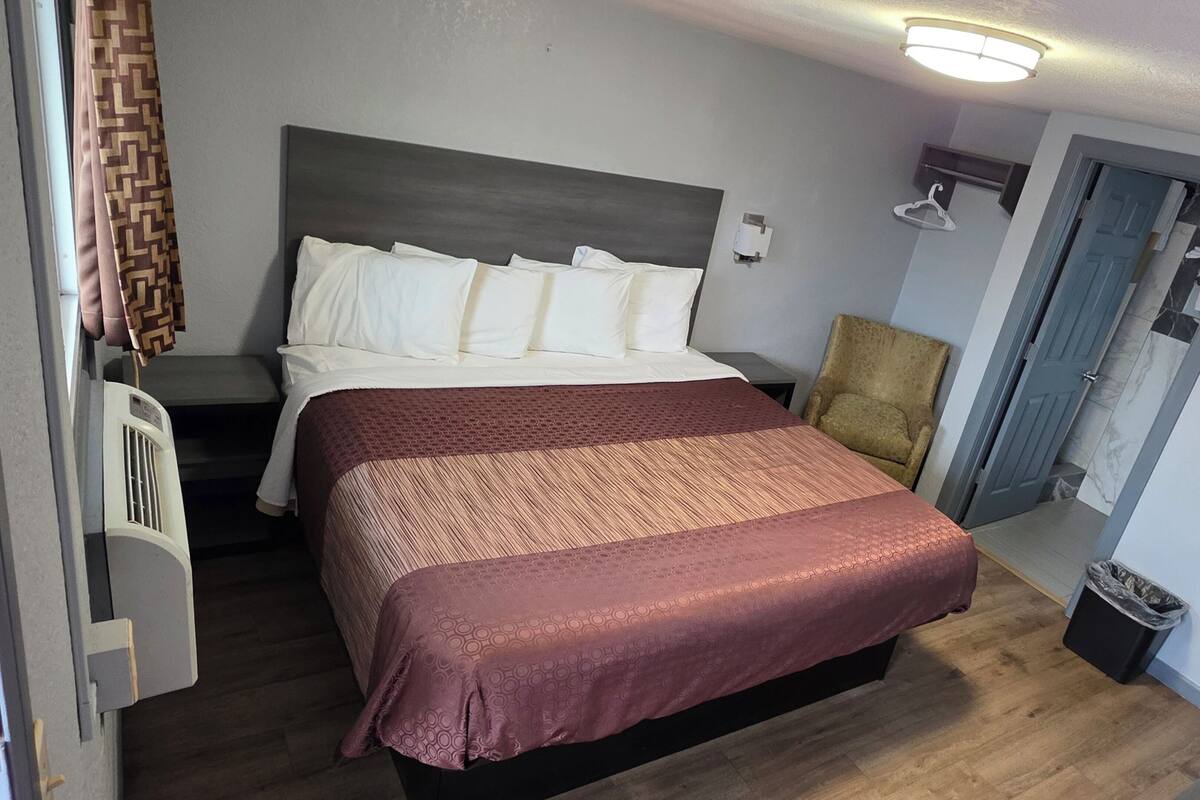 A bedroom with a bed, a chair, a wall-mounted light, and a door.