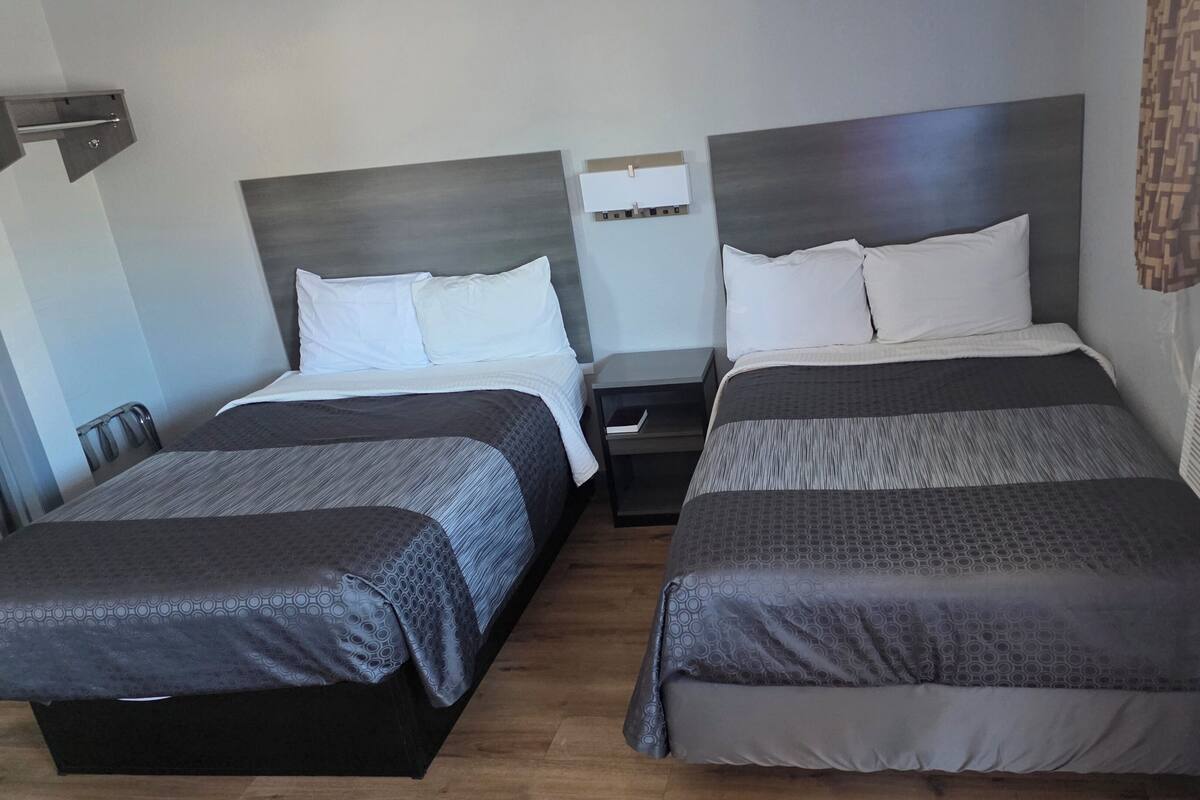 A double room with two beds, a bedside table, a small shelf, and a window with curtains.