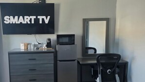 A modern room with a desk, chair, refrigerator, microwave, and a TV labeled 'SMART TV.' - Plaza Motel (Joplin)