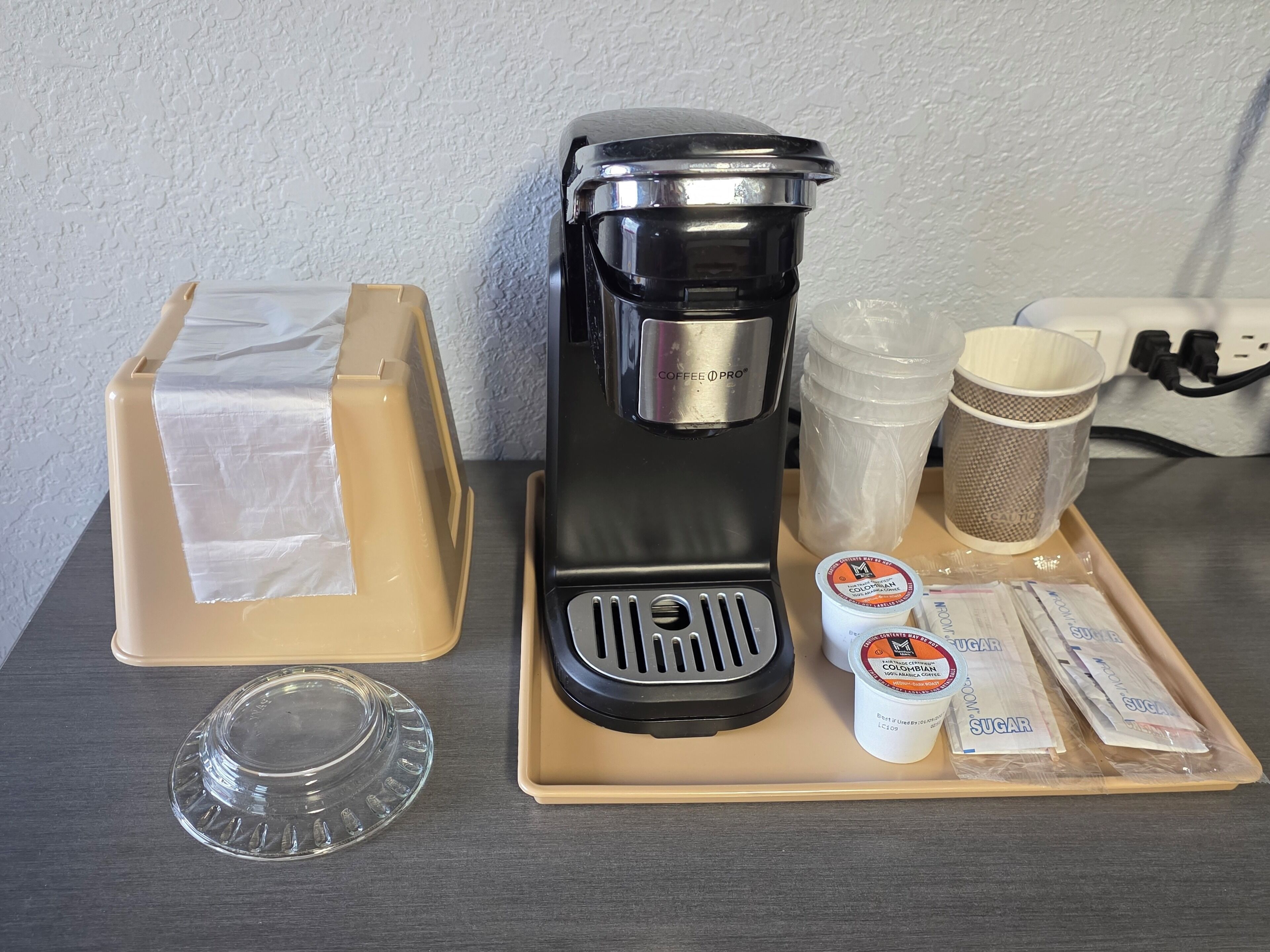 Una cafetera, una cápsula de café, un sobre de azúcar, un espumador de leche y una jarra de vidrio sobre una bandeja.