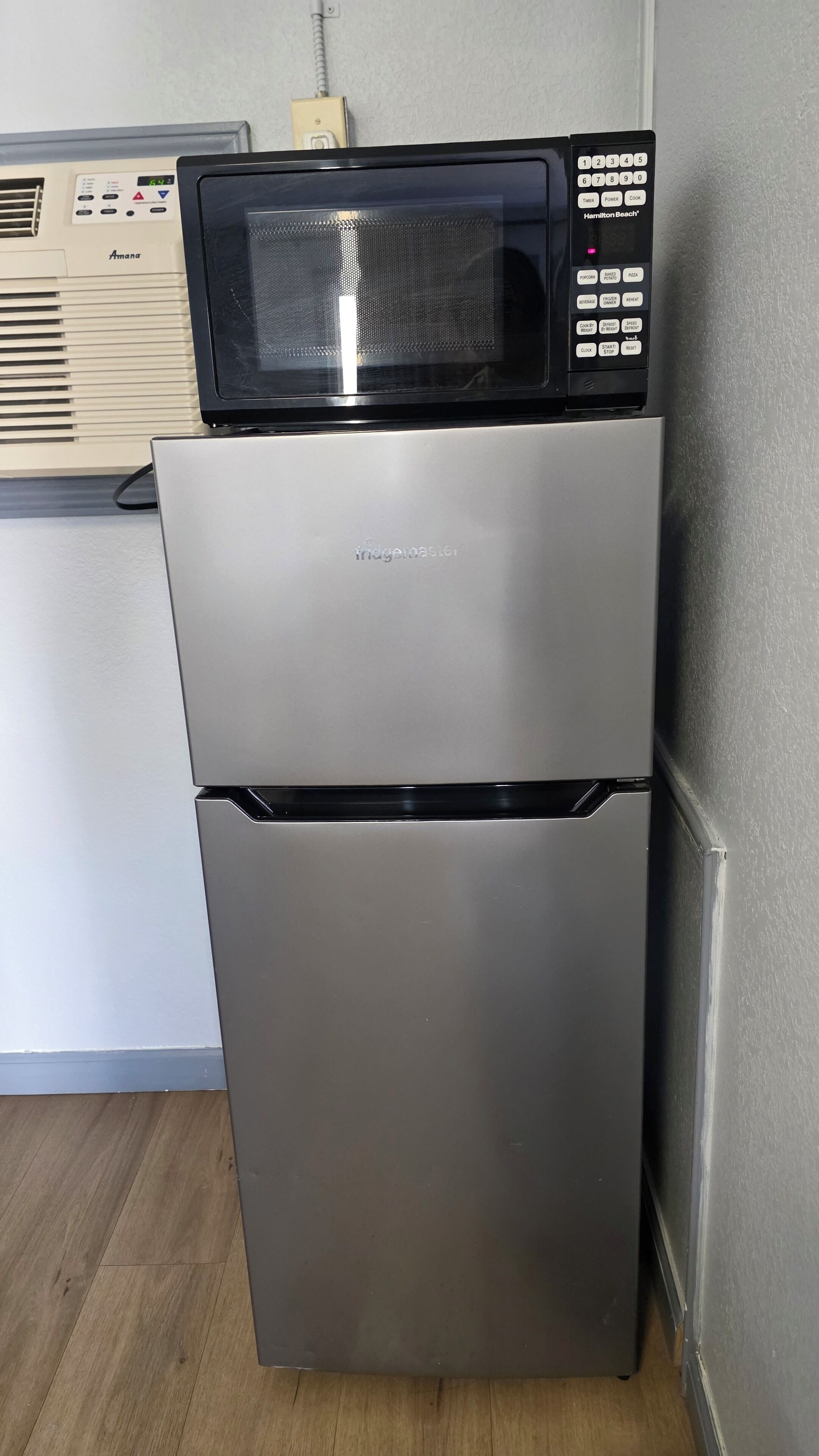 Un refrigerador de acero inoxidable con un microondas encima, un panel de control y un cajón congelador.