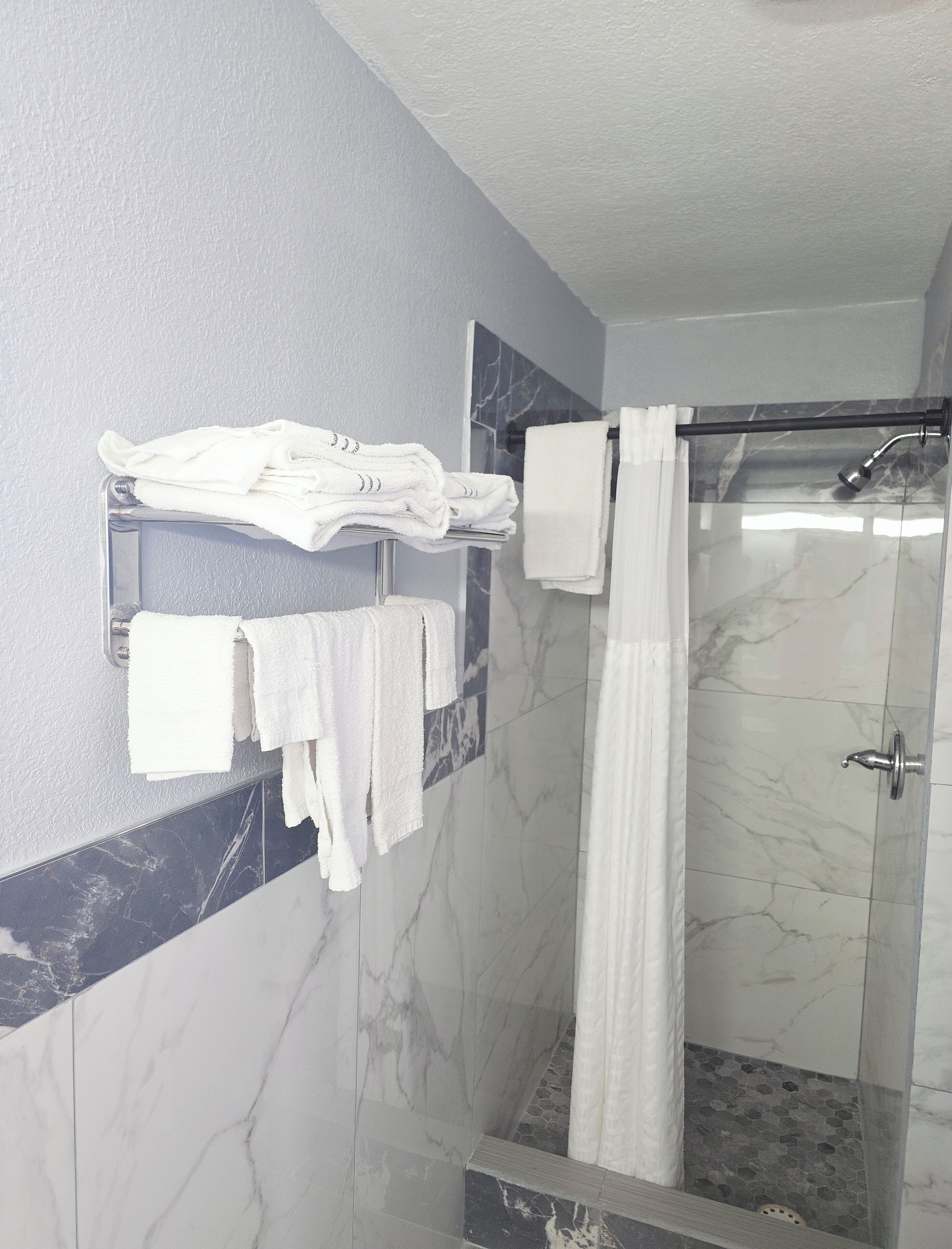 Un baño con cabina de ducha de vidrio, paredes de mármol y un perchero con toallas dobladas.