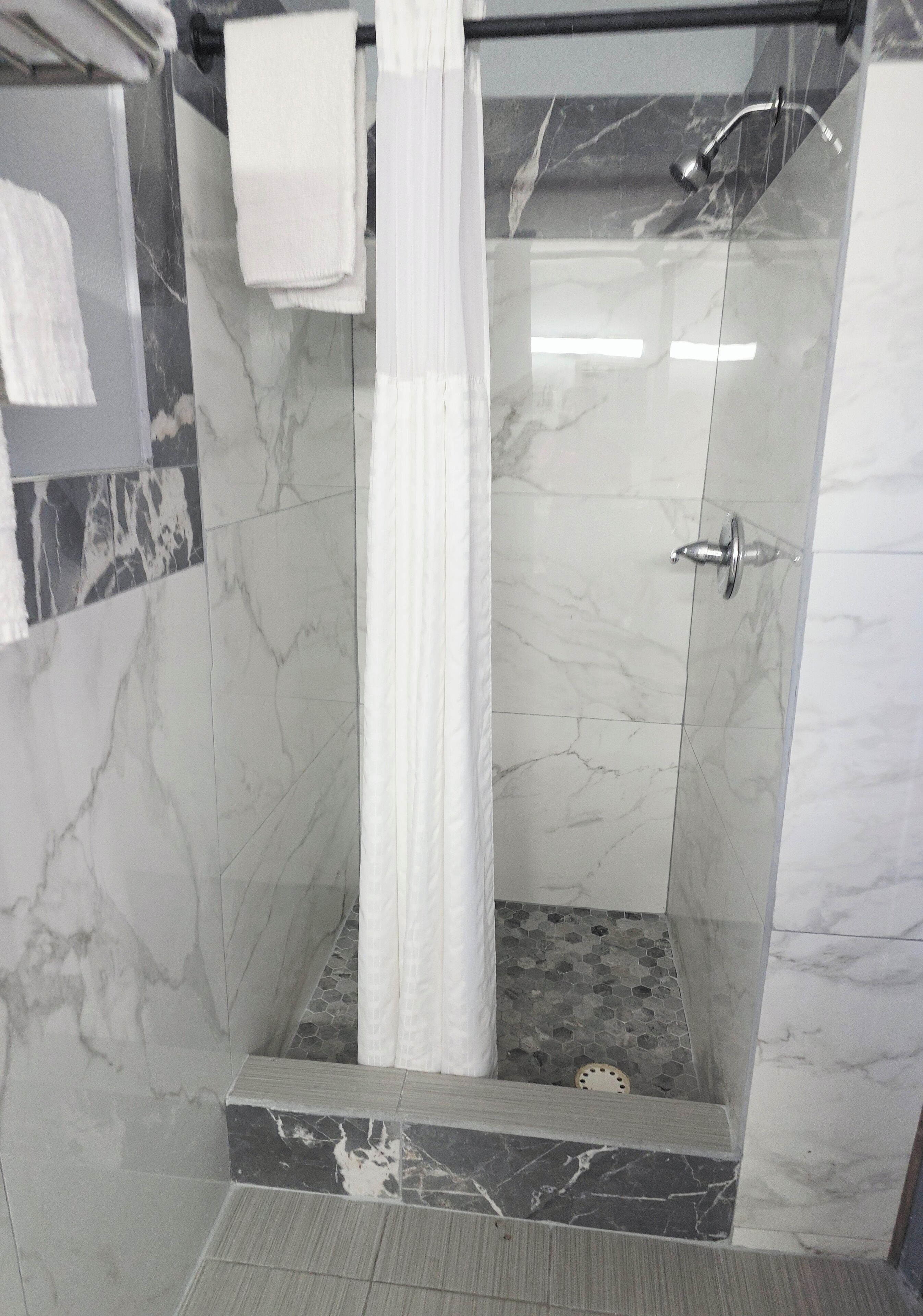 Ducha con puerta de vidrio, una toalla blanca colgada en la pared y suelo de baldosas con diseño de mármol.