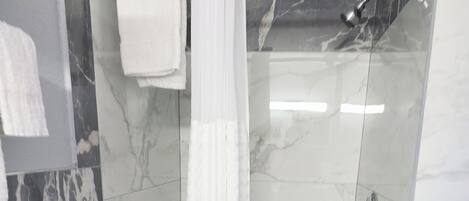 Ducha con puerta de vidrio, una toalla blanca colgada en la pared y suelo de baldosas con diseño de mármol.