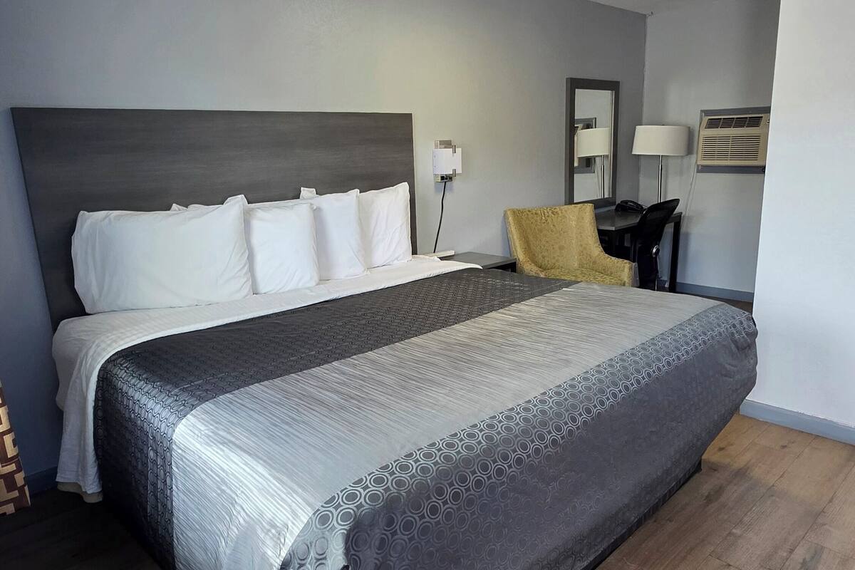 A modern hotel room with a large bed, a desk, a chair, and a mirror.