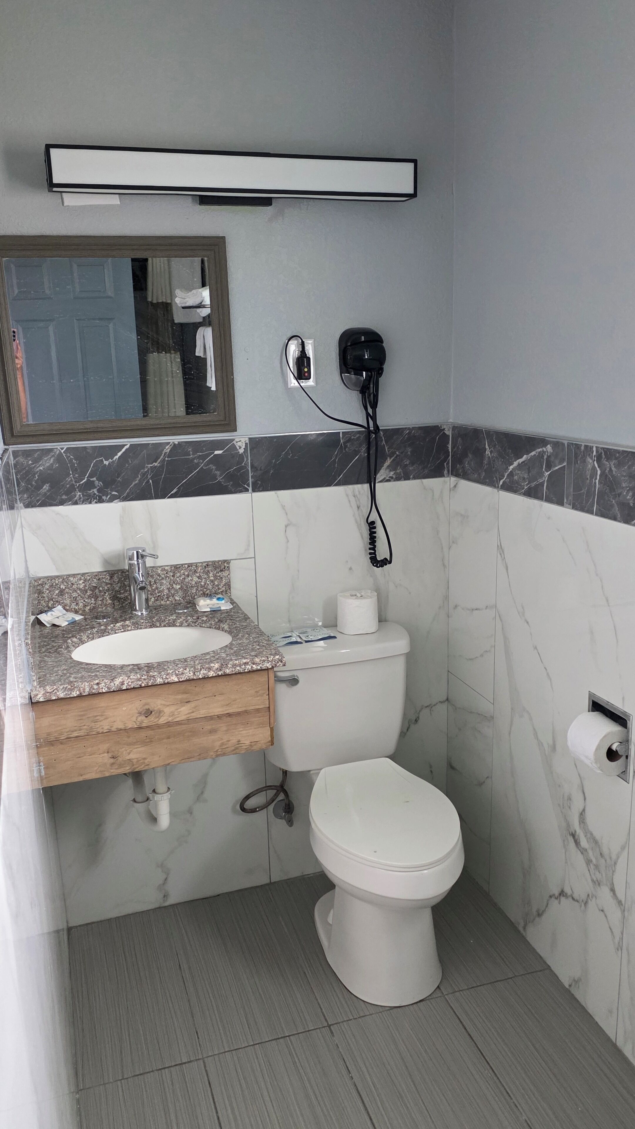 Un baño con pared de mármol, un lavabo con encimera de madera, un inodoro y un secador de pelo en la pared.