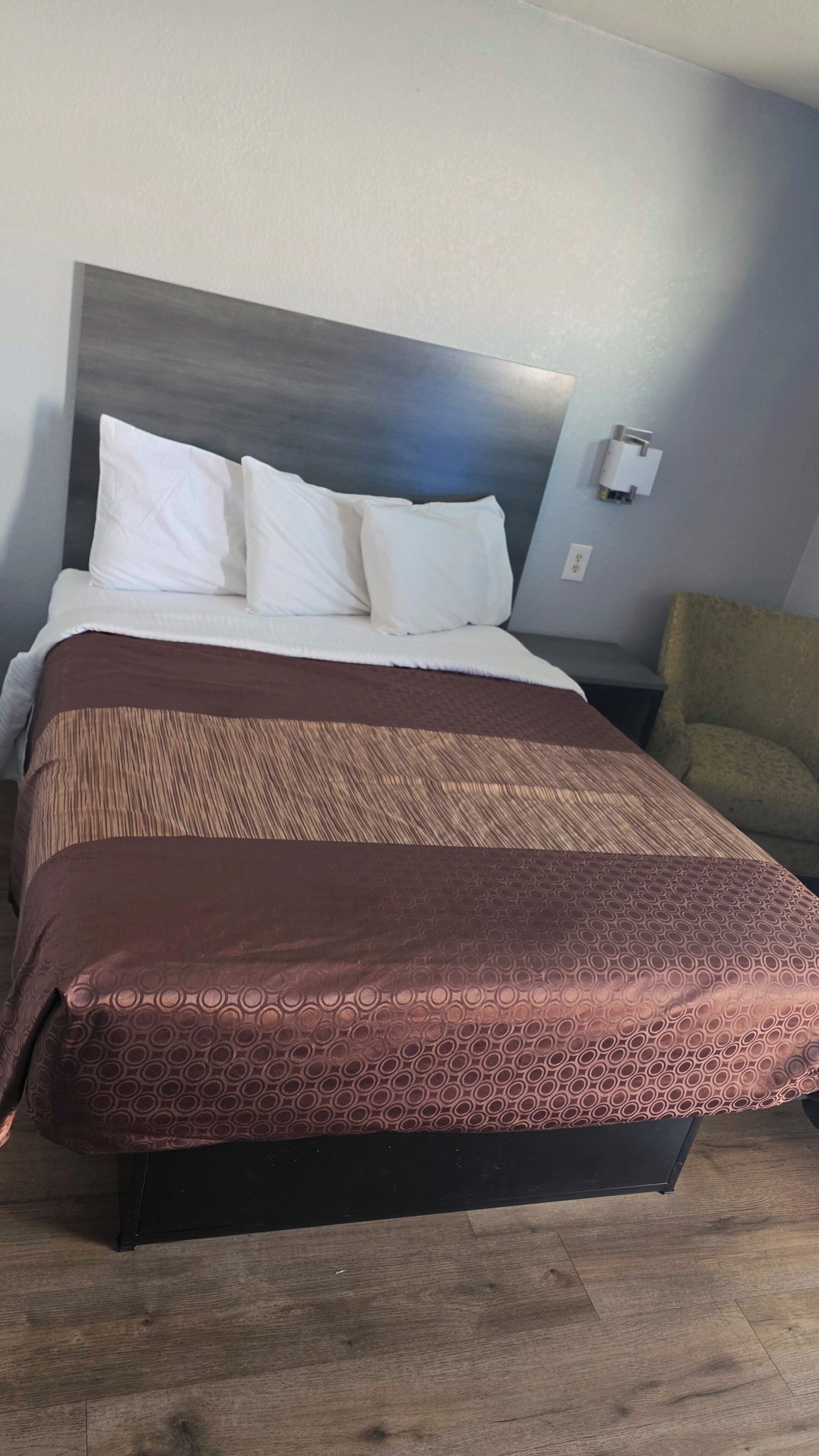 Une chambre d’hôtel avec un lit, une tête de lit, une table de chevet et une chaise.