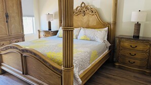 Ein Himmelsbett mit floralem Überwurf, ein Nachttisch aus Holz mit Schubladen und ein großer Kleiderschrank.