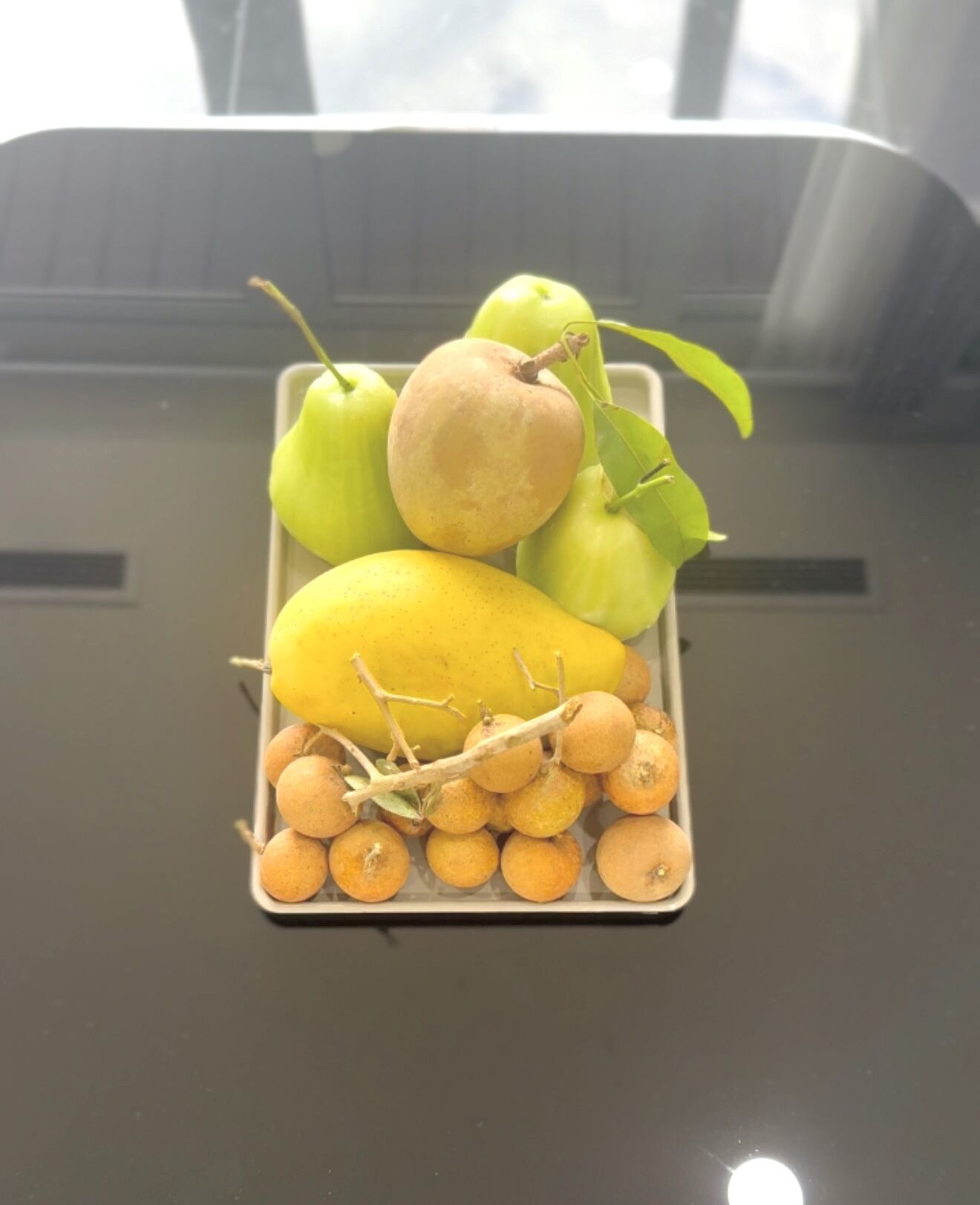 A fruit tray with apples, a pear, a lemon, and small round fruits on a table.