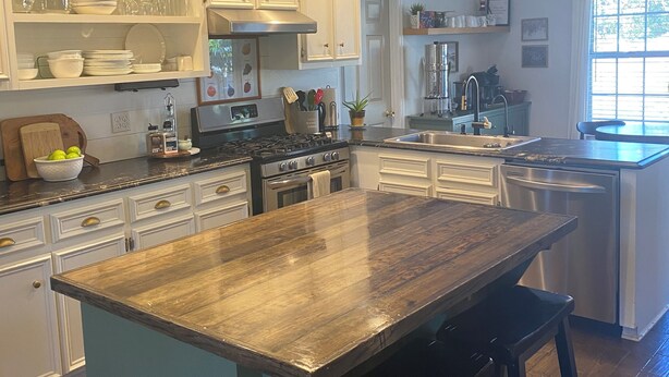 A modern kitchen with white cabinetry, a central island with stools, pendant lighting, and a view of the outdoors through a large window.