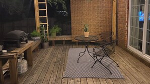 A wooden deck with a grill, potted plants, a table with chairs, and string lights.