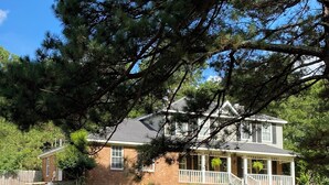 A two-story house with a brick exterior, a front porch with white railings, and a well-maintained lawn.