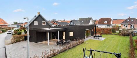 A modern building with a covered patio area, a swing set, and a small play area with toys.
