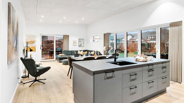 A modern kitchen with a central island, large windows, and a dining area with a sofa and chairs.