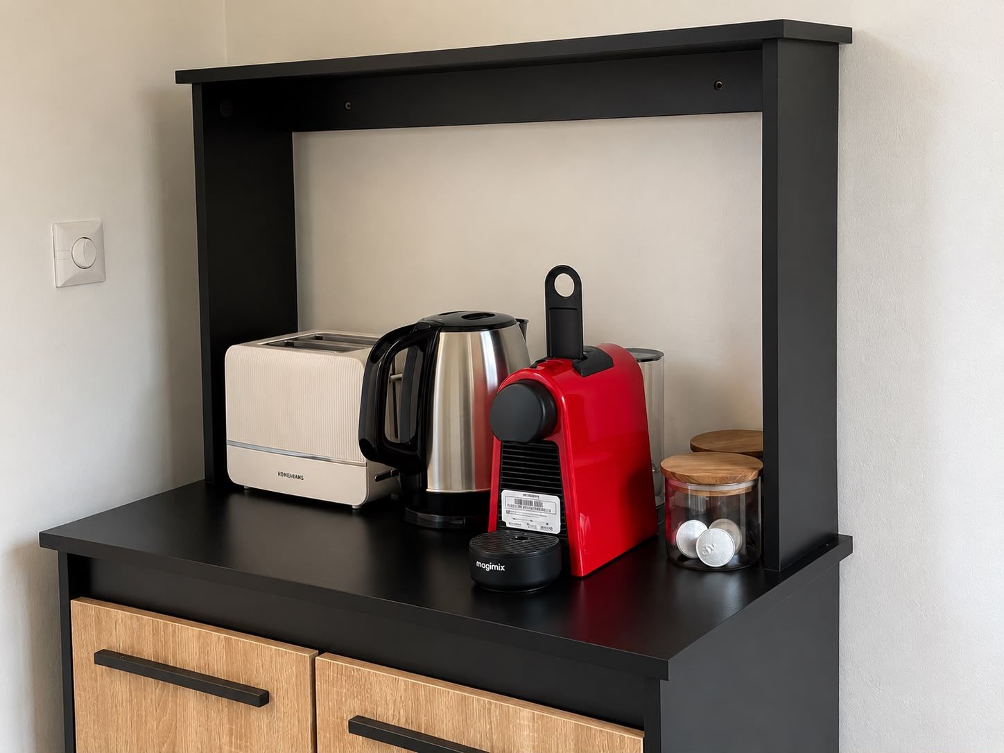 A kitchenette with a toaster, a coffee maker, a kettle, and a jar of sugar on a black countertop.