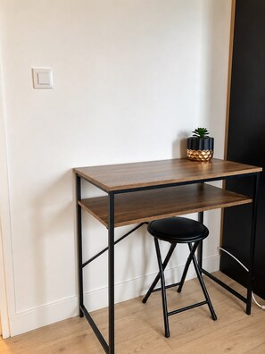 Ein kleiner, dunkler Holztisch mit schwarzem Metallgestell, ein schwarzer Hocker und ein Blumentopf darauf.