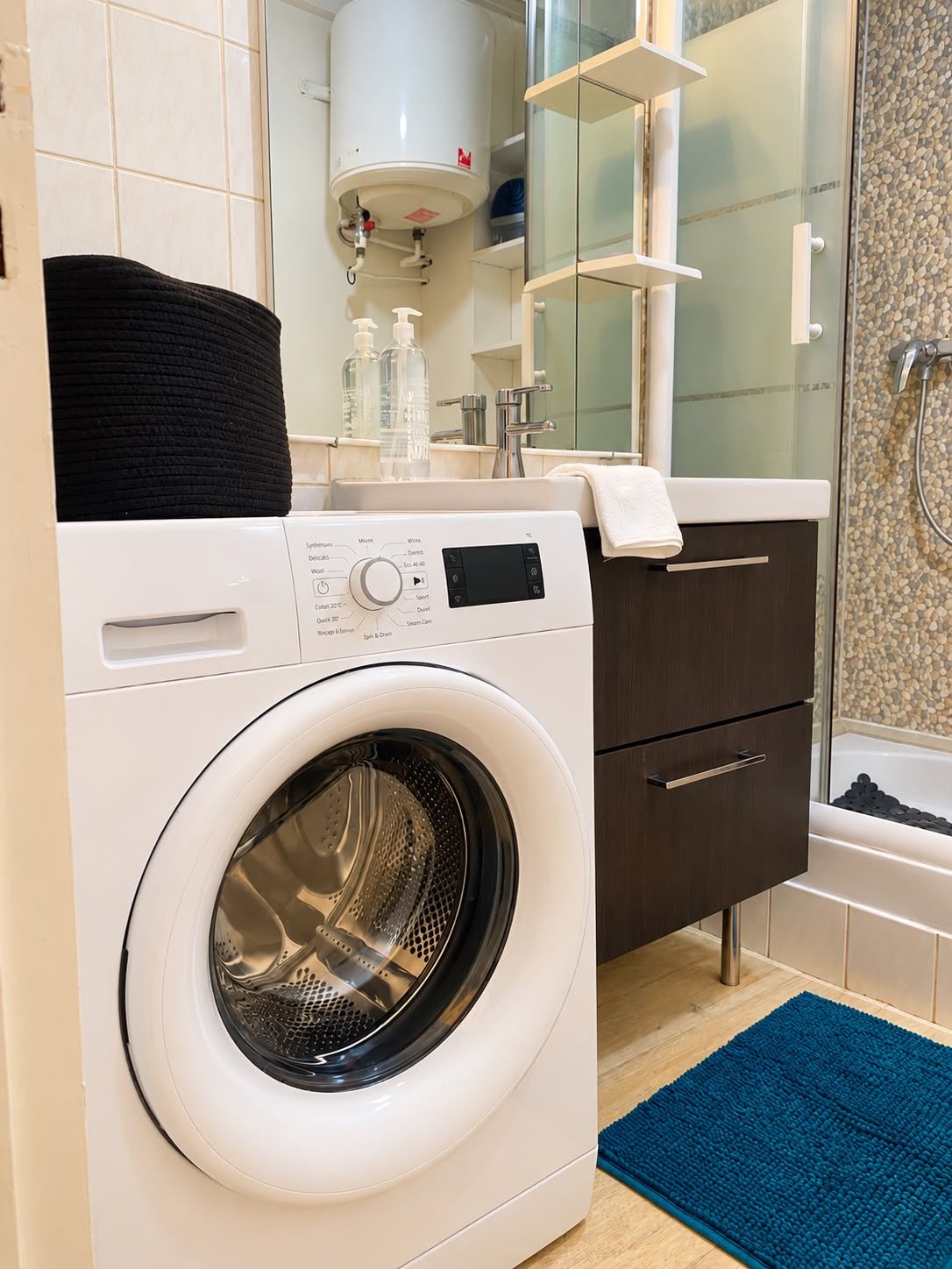 A modern bathroom with a built-in washing machine, a glass shower enclosure, and a wooden vanity.