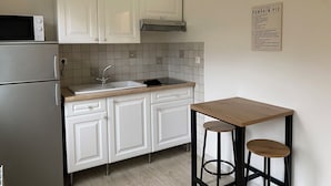 A compact kitchen with white cabinets, a microwave, a sink, and a small wooden table with stools. - Cosy studio in Évreux - Ideal! (Évreux)