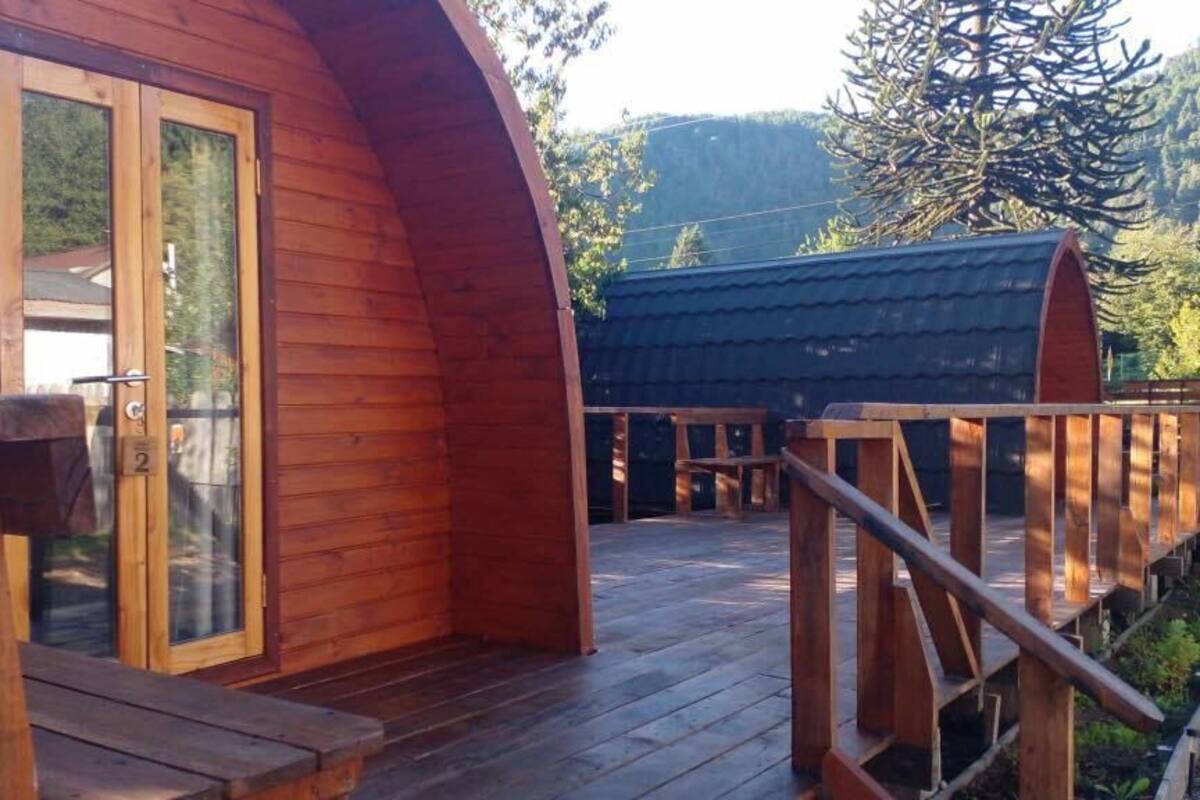 Eine Holzhütte mit gewölbtem Dach, einer Holzterrasse und einer Glastür.